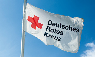 Fahne mit Rotkreuzsymbol vor blauem Himmel